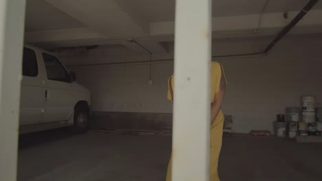 carefree and cheerful alternative woman in loose dress and expressive makeup dancing behind iron bars in the garage