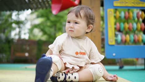 curious baby girl with knee pads sitting and playing in an outdoor playground