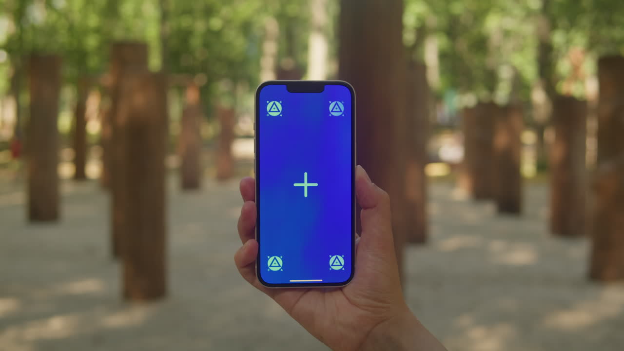Young woman holding phone chroma key screen in front of playground close-up. Girl with green screen on smart phone. Nature