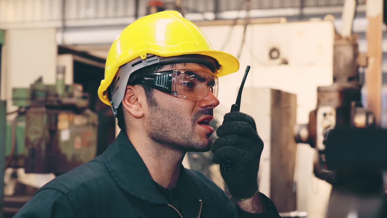 trabajador de una fábrica hablando por radio portátil mientras inspecciona piezas de maquinaria