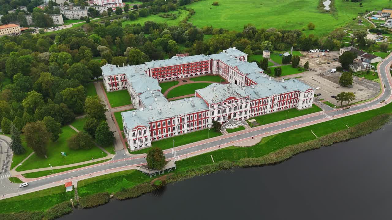 Jelgava Palace beside the Lielupe River revealing baroque architecture green lawns and tree-lined paths in a historic Latvian landscape, drone ascends and pulls away