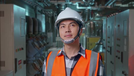 close up of asian male engineer with safety helmet looking around while standing in engine control room, work of electrical generators