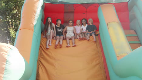 slow motion shot of group of children playing on inflatable slide at summer garden fete