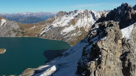 Un-Hombre-Está-Solo,-Mirando-Las-Montañas-Cubiertas-De-Nieve-Y-El-Lago-Turquesa-Debajo-De-él