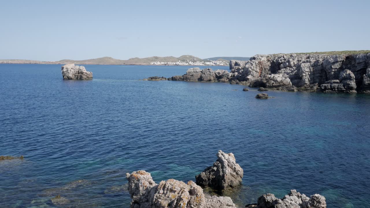 Clear blue water with rocky coastline and distant hills at Cala Viola De Llevant
