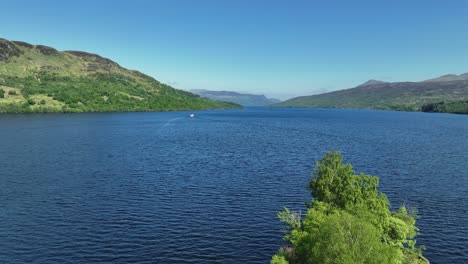 aerial shot of loch katrine in the trossachs national park in scottish highlands, scotland during hot summers day with ferry in distance