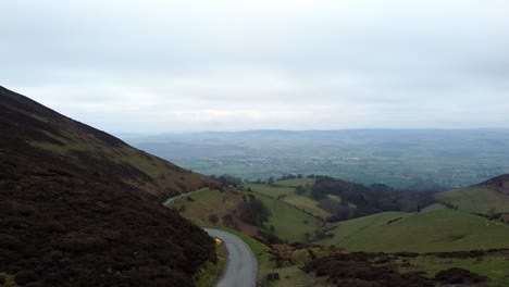 Narrow-single-rural-road-running-through-Welsh-green-mountain-valleys-landscape-low-aerial-dolly-view-left