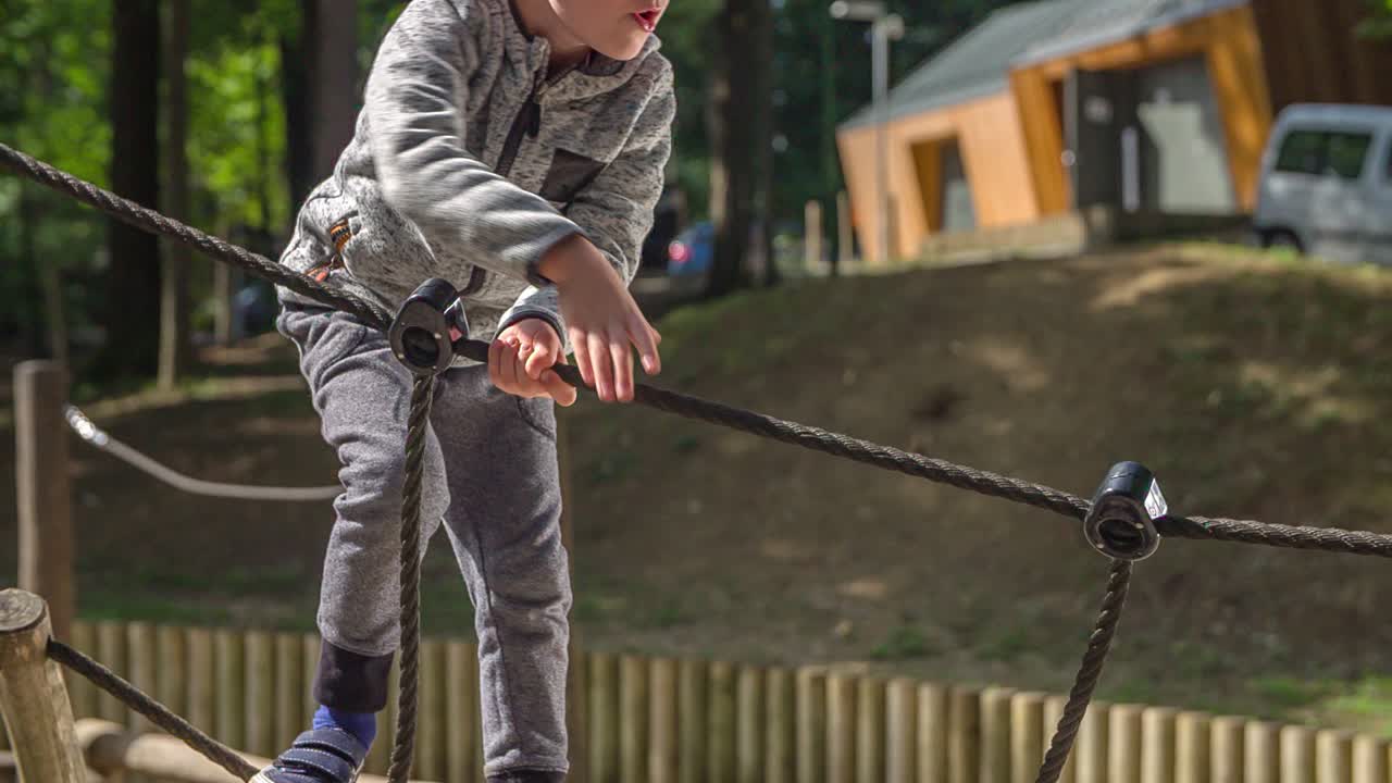 A young boy playing on a playground, climbing ropes and wood and practicing his balance in an adventure park