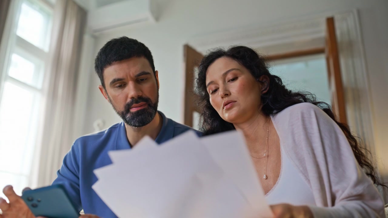 Coppia preoccupata che controlla le bollette a casa. Marito e moglie incinta che esaminano documenti
