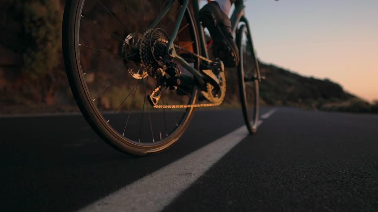 The athlete on a bike is captured in slow motion riding a mountain serpentine, enjoying the island's view, embodying dedication to a healthy lifestyle at sunset