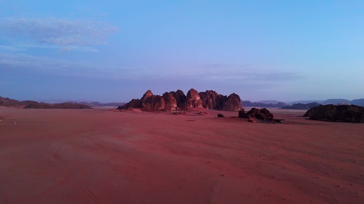 Ripresa con drone del deserto del Wadi Rum all'alba, con la prima luce del giorno che illumina le frastagliate montagne di arenaria e la sabbia rossa.