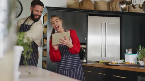 video de una feliz pareja caucásica usando una tableta en la cocina