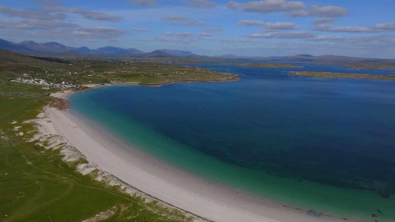 Dog's Bay Beach, Roundstone, Connemara, County Galway, Ireland, May 2025. Drone orbits clockwise aerial view of clear turquoise waters, white sand and Twelve Bens mountain range in wild Atlantic way