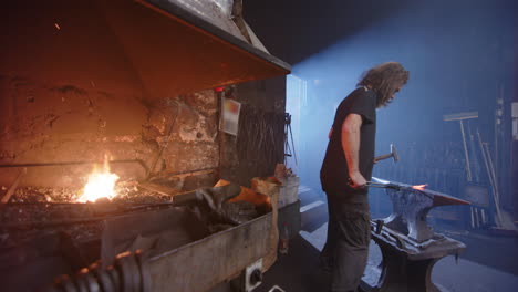 long haired blacksmith removes his glowing piece from the forge to work on anvil