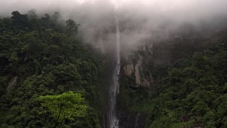 waterfall cascading down a high, rocky cliff face along the trail to quebrada gata. the surrounding lush, green rainforest is partially obscured by fog, creating a mystical and immersive atmosphere