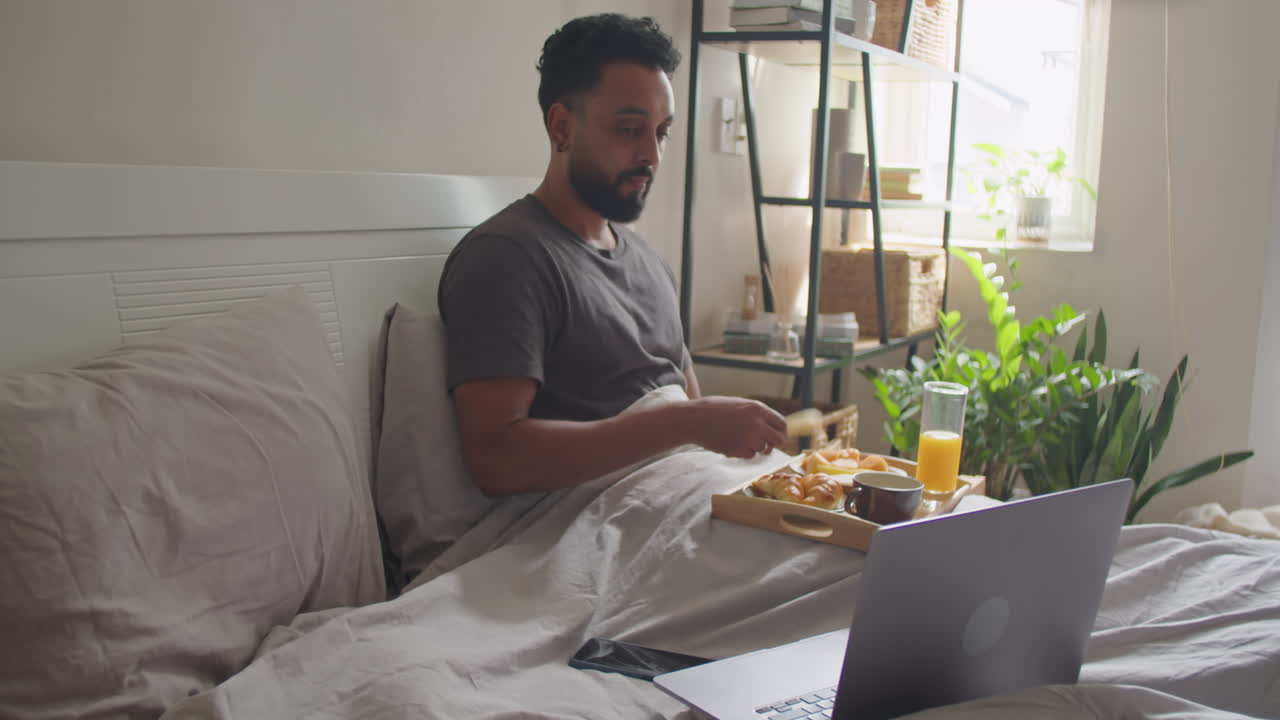Man Having Breakfast in Bed and Using Laptop
