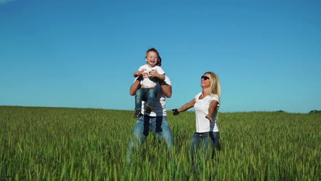 glückliche familie: vater, mutter und sohn springen und lachen auf dem feld in weißen t-shirts und jeans