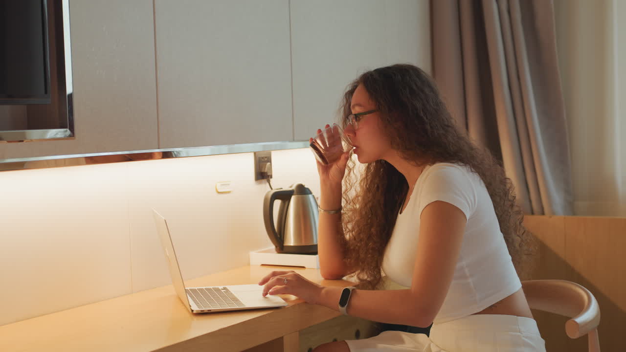 Student works diligently. Young woman focuses on studies. Young lady concentrates on her laptop during quiet morning. Female student engaged in focused study session with notes and warm light