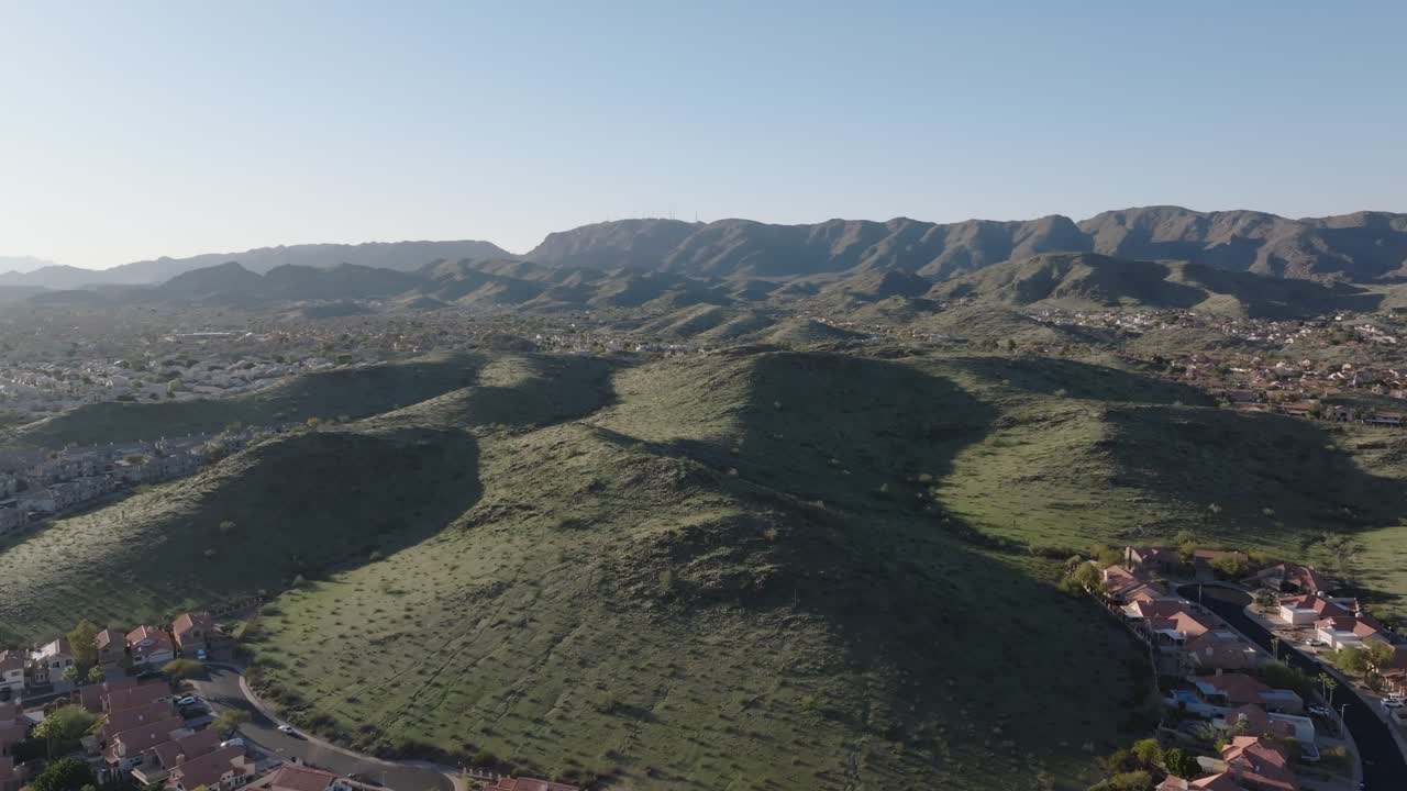 colinas verdes rodeadas de vecindarios y montañas lejanas bajo un cielo azul claro