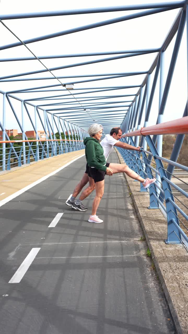 Seniorenpaar dehnt sich und trainiert auf einer modernen Stadtbrücke