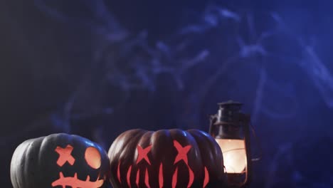 Video-of-halloween-carved-pumpkins,-candles-and-smoke-with-copy-space-on-blue-background