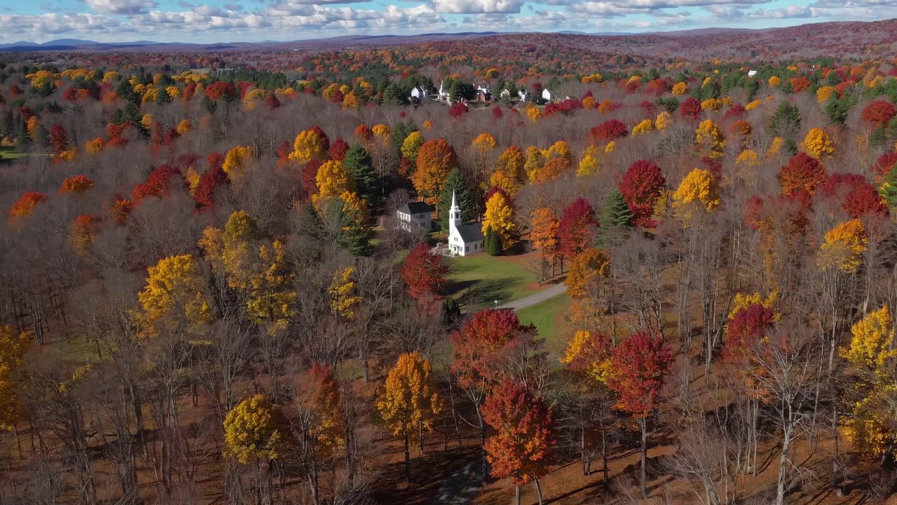 Aerial video captures a vibrant autumn landscape with colorful trees and a quaint church