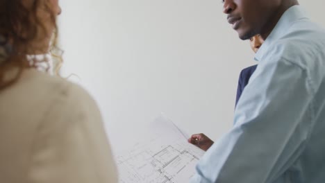 biracial male and female architects checking architects plans in modern office