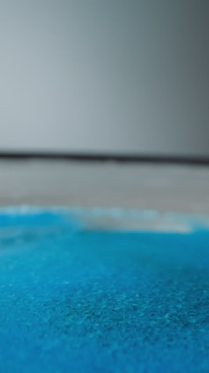 Pile of blue hydrophobic sand lies on convex rounded surface on gray background. Bright small particles for creation decorative elements and children games macro