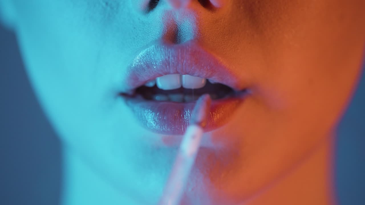 acercamiento extremo de una mujer joven y bonita aplicando brillo de labios brillante en sus hermosos labios mientras se prepara para salir con amigos para una noche de club o una cita con contraste naranja turquesa en su cara