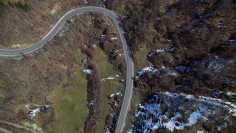 Top-down-shot-of-cars-navigating-a-winding-road-through-Romania’s-mountainous-terrain