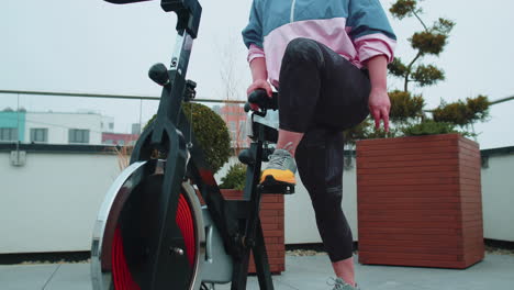 chica atlética realizando ejercicios de entrenamiento de equitación aeróbica en bicicleta bicicleta estacionaria en el techo de la casa