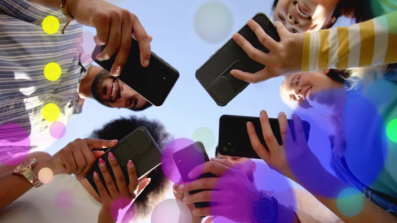 Five adults circling low cam tapping phones sharing social content causing colored circles drifting