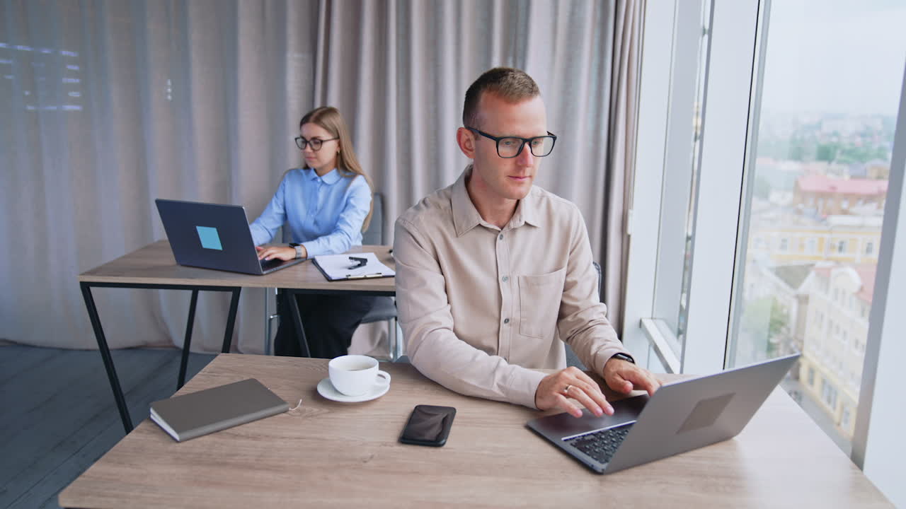 People working on computers at their desks in the office. Modern office work in a light room with big panoramic window.