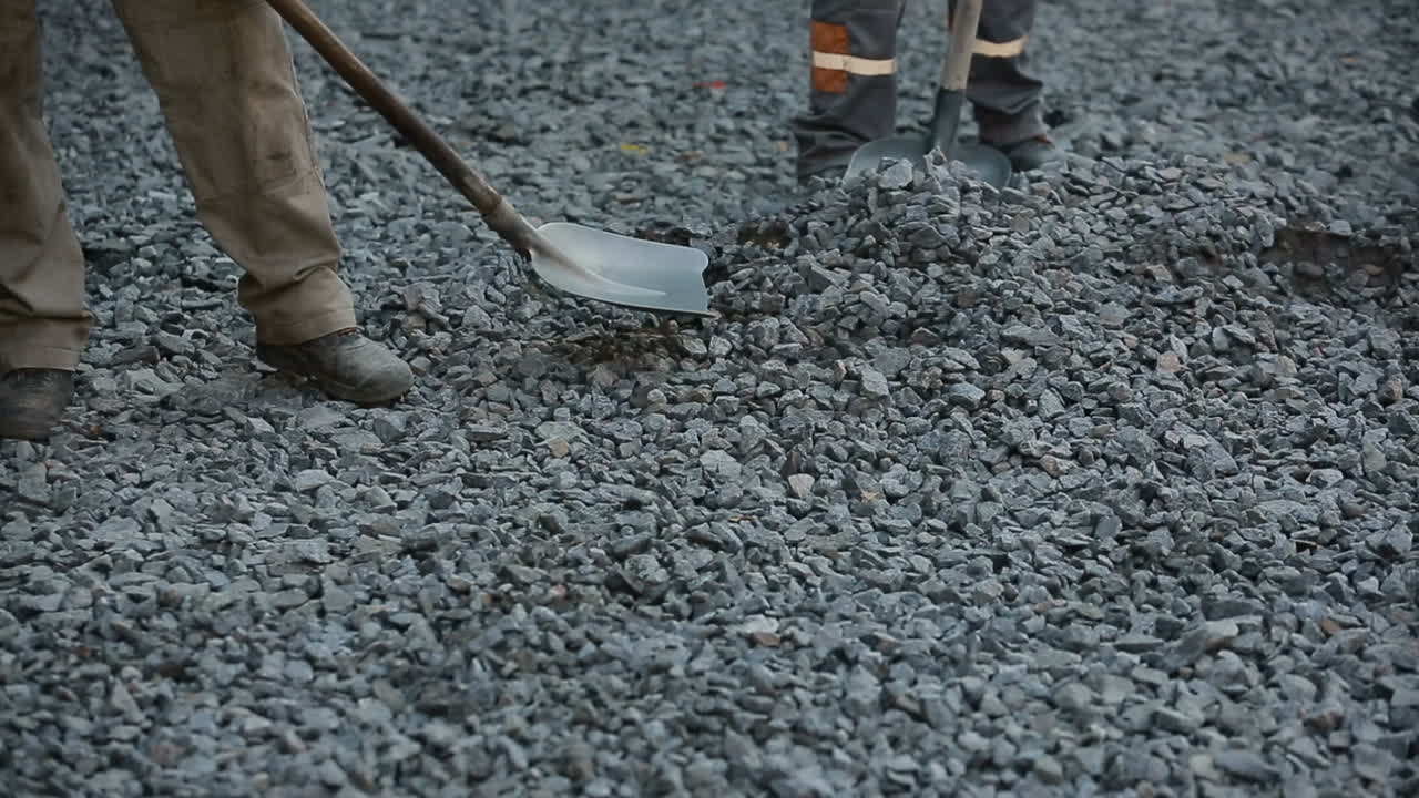 Construction worker holding shovel with gravel working on road construction