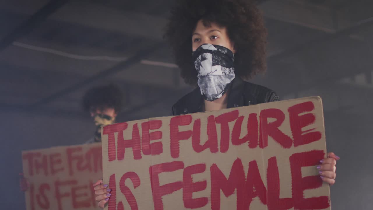 hombre y mujer de raza mixta con máscaras faciales sosteniendo carteles de protesta