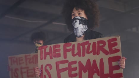 mixed race man and woman wearing face masks holding protest signs