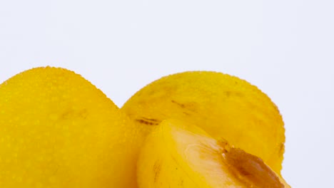 macro shooting of two whole and one half cut of a big yellow plums with the pit. slowly rotating on the turntable isolated on the white background. close-up