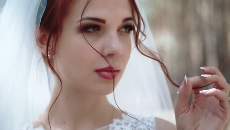 Portrait-of-a-bride-in-a-forest-in-a-wedding-dress-that-touches-a-curl-of-her-hair-close-up-slow-motion