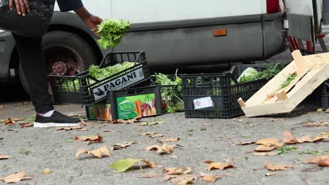 Vista-De-Cerca-De-Una-Mujer-Negra-Buscando-Y-Recogiendo-Comida-Sobrante-Después-De-Un-Mercado-Callejero-En-Milán,-Italia