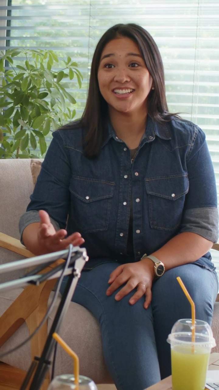 Vertical video: Mic boom entering woman in denim shirt speaking, gesturing for podcast, green cup