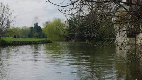water flows down calm river as tour guide pushes boat by beautiful grass and building