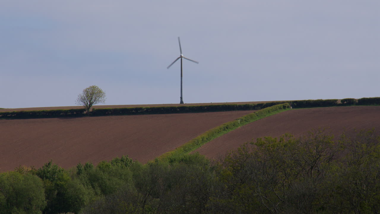 Wide shot of a single wind turbine on top of the hill with farmland in Foreground in the Teifi Estuary at St Dogmaels