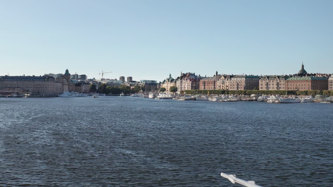 Drone shot flying over body of water toward Nybrokajen and Strandv&auml;gen in Stockholm, Sweden during sunny evening