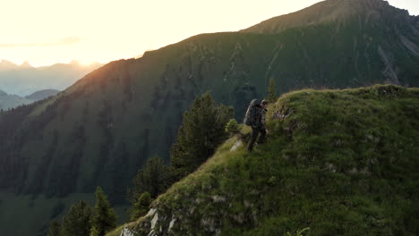 beautiful cinematic aerial shot of lone professional mountain hiker going on top of mountain peak at sunrise