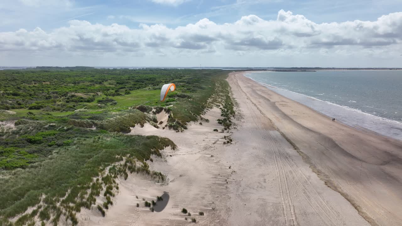 vista épica de la grúa de drones del parapente solitario a la deriva sobre las exuberantes dunas de arena junto al mar