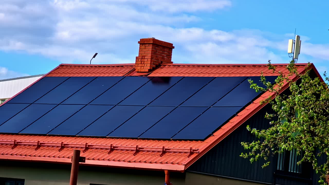 Rooftop solar panels installed on red metal house roof with chimney under blue sky