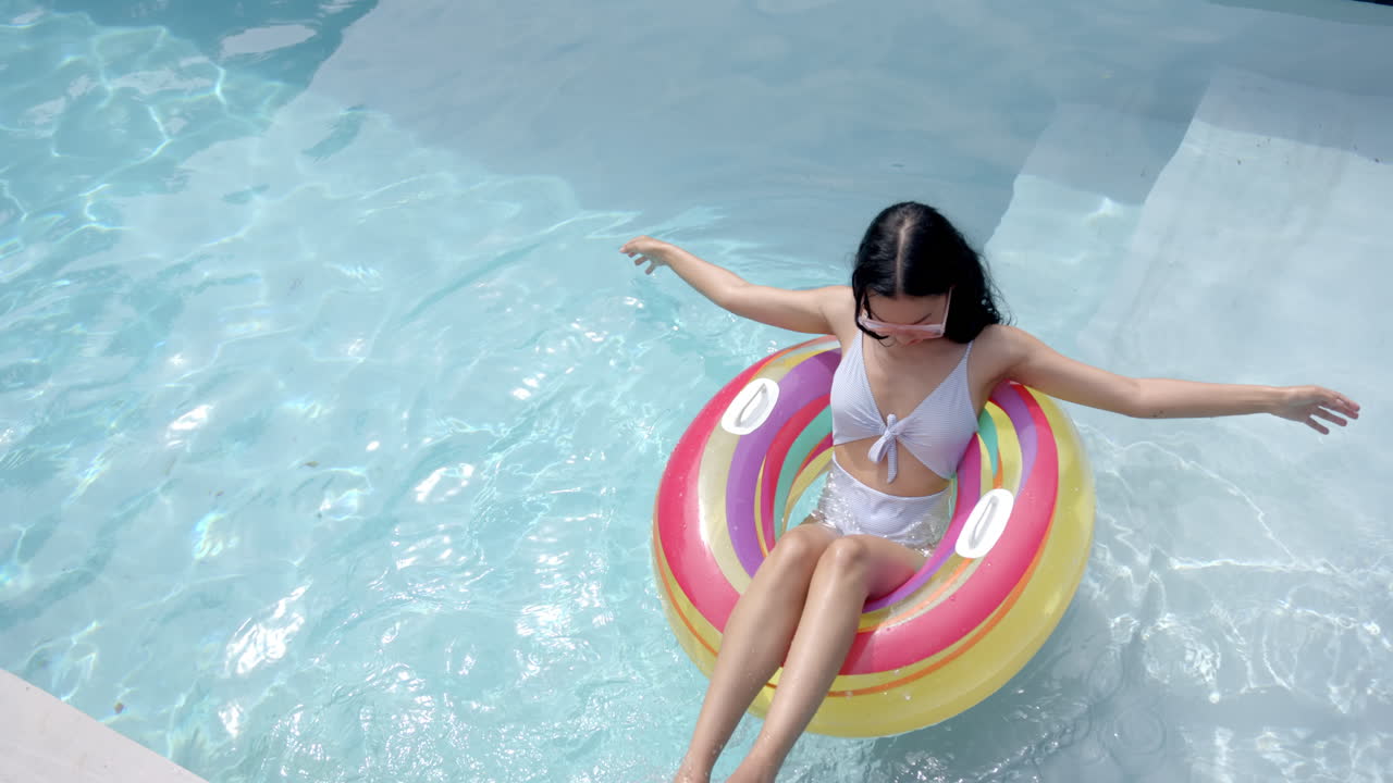 A young biracial woman lounges on a colorful pool float