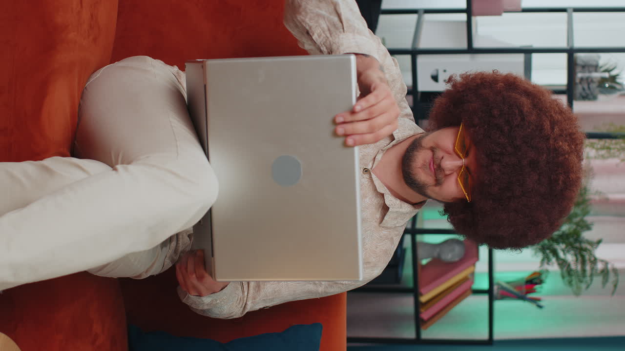Young man freelancer sitting on sofa closing laptop pc after finishing work in living room at home