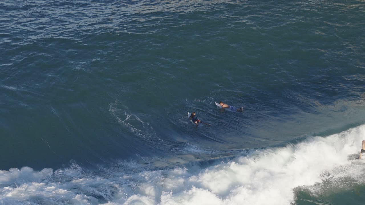 Drone captures surfers navigating waves at Gold Coast, Australia. Clear skies, dynamic movement, and vibrant ocean colors create an energetic scene