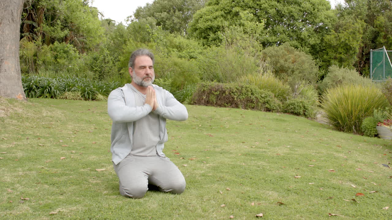 Mature man meditating outdoors on grass, practicing mindfulness in nature, copy space